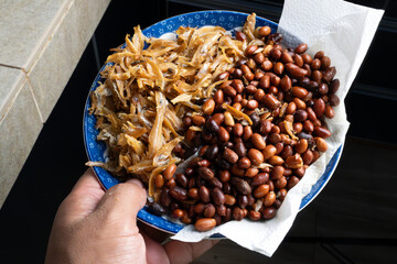 A close-up view of a traditional Malaysian side dish featuring crispy fried anchovies (ikan bilis)...