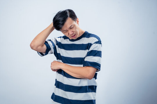 Asian man in navy and white striped t-shirt scratching his head with frustrated expression, standing against plain light background, representing confusion, regret, or problem-solving moment