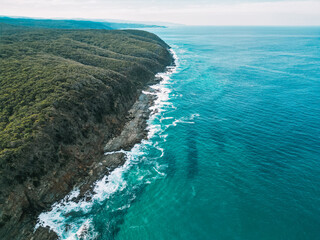 Aerial view of stunning turquoise water along a rocky coastline in Victoria, Australia. Crystal-clear ocean waves meet rugged cliffs, creating a breathtaking coastal landscape. Scenic natural beauty
