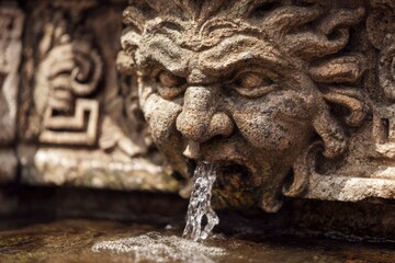 Stone face fountain head with water flowing from its mouth into a pool Detailed carving ancient look