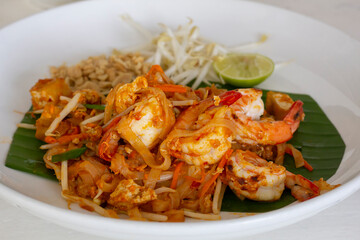 Close up Stir Fried Rice Noodle Thai style with Prawns, side dishes and condiments or Thai people call Pad thai in plate on the table in the restaurant.