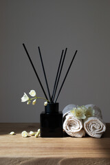 Modern composition of perfume in black glass diffuser with sticks decorated flowers and towels for home aromatherapy.