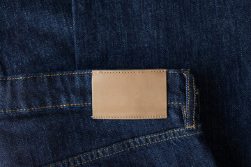 Empty leather tag or label on blue denim jeans clothes top view. Shopping, sale and fabric industry background.