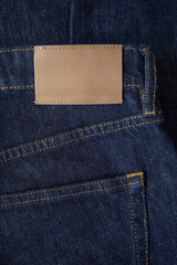 Empty leather tag or label on blue denim jeans clothes top view. Shopping, sale and fabric industry background.