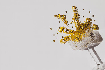 Champagne glass, serpentine and golden stars on white background. Shiny greeting card for Christmas, wedding or birthday party.