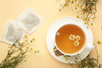 Aromatic herbal tea in white cup and chamomiles on beige background. Space for text