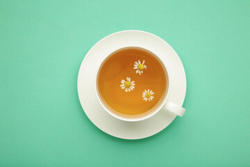 Aromatic herbal tea in white cup and chamomiles on mint background.