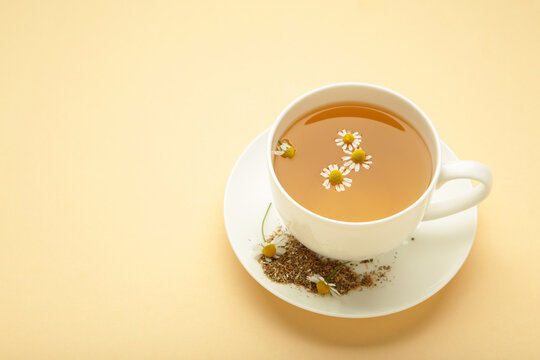 Aromatic herbal tea in white cup and chamomiles on beige background. Space for text