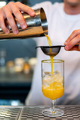 A bartender skillfully pours a vibrant yellow cocktail through a strainer into a glass filled with ice, capturing the moment of mixology precision in a bar setting.
