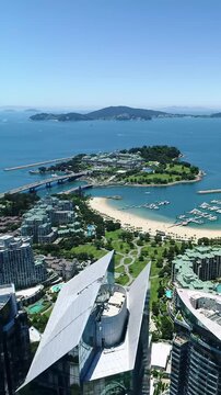 God's eye view of a sun-drenched, luxurious coastal city resort: modern skyscrapers, pristine beach, bustling marina with yachts, palatial building on peninsula over azure ocean, distant islands.