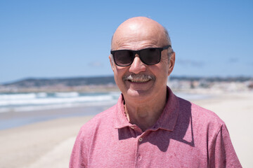 An elderly man with a mustache walking on the beach, enjoying his vacation.