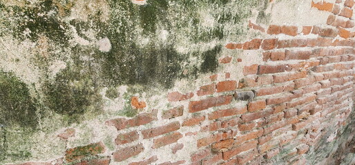 Antique red brick background. Old brick wall with some moss. Peeling wall revealing red brick inside. Outdoor cement fence damaged by sun and rain. 
