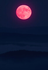 Fototapeta premium Vibrant red full moon glowing in dark night sky above misty forest landscape, creating mysterious and serene atmosphere