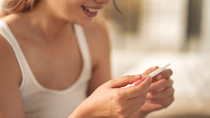 A woman holding a pregnancy test. She is smiling and she is happy about the result