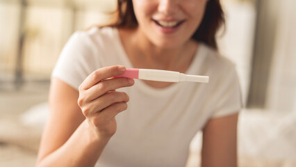 A woman holding a pregnancy test. She is smiling and she is happy about the result