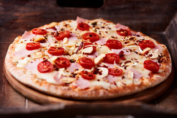 Pizza with ham, cherry tomatoes and mozzarella cheese. Wooden background. Soft focus. Close up.	