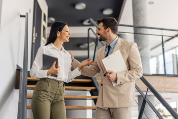 Cheerful elegant businesspeople standing on stairs in minimalistic workspace and discussing.