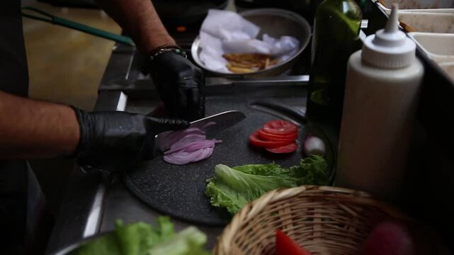 A cheff cutting onion to prepare a cheese burger
