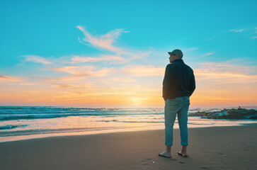Barefoot man admiring a beautiful sunset over the ocean, finding peace and inspiration on a sandy...
