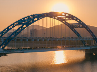 Naklejka premium Evening panorama of a blue arch bridge with moving cars over calm water at sunset. Hangzhou, China.