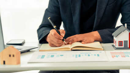 Real estate agent using laptop at desk with miniature model of house, representing real estate investment, buying a house, close up.