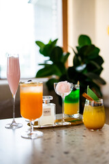 A vibrant selection of cocktails in various colors, elegantly arranged on a table. The image features layered drinks, garnishes, and a stylish perfume bottle for a refined aesthetic