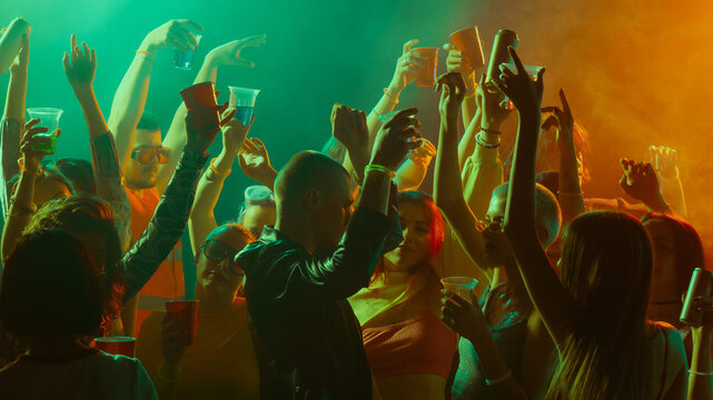 Vibrant party scene with people dancing and celebrating under colorful lights. Concept of nightlife, party, youth, summer, festivity, celebration