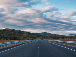 A long, open highway leads through a picturesque mountainous area.