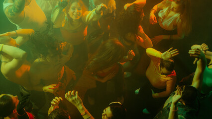 Top view of people dancing energetically in colorful lighting. Concept of nightlife party, youth, summer, festivity, celebration