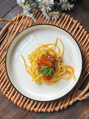 A serving of spaghetti adorned with a rich tomato-based sauce, garnished with fresh herbs. Presented on a white plate, it showcases the delicious combination of Italian-inspired flavors and textures.