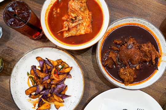 Top view of variety of dishes to be eaten with rice, namely asam pedas kepala ikan merah, ayam masak kicap and terung goreng lada.