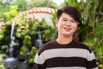 Young cute gay man in Zen style garden park with waterfall relaxing