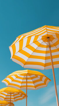 Yellow and white striped beach umbrellas standing tall against a clear blue sky