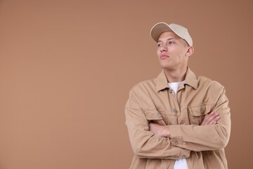 Young man wearing stylish beige baseball hat on light brown background, space for text