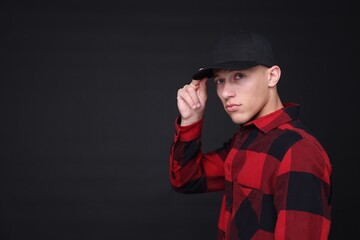 Young man wearing stylish baseball hat on black background, space for text