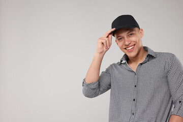 Young man wearing stylish black baseball hat on light grey background, space for text
