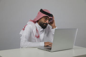 A Saudi Arabian man wearing traditional dress using a laptop, expressing different...