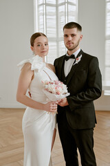 Portrait of Caucasian young adult woman in wedding dress holding bouquet standing beside Caucasian...