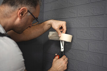 Man sticks protective tape on the wall before painting