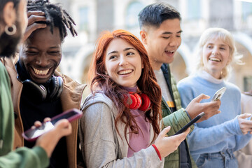 Group of diverse young friends smiling and interacting with smartphones in spontaneous urban moment