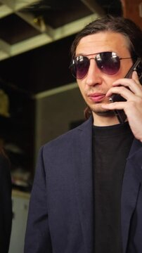 This footage conveys a cool and intriguing mood, depicting a person on a phone call while adjusting their sunglasses, suggesting a moment of discreet communication or a sophisticated persona