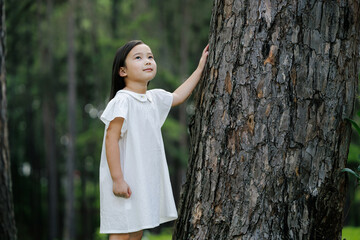 A child gently touches a tree in a lush forest, symbolizing connection to nature, environmental awareness, and future sustainability.
