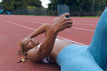 Female runner lying on the track taking a selfie on her mobile phone