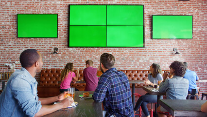 People Sitting At Tables In Sports Bar Watching Game On Green Screens