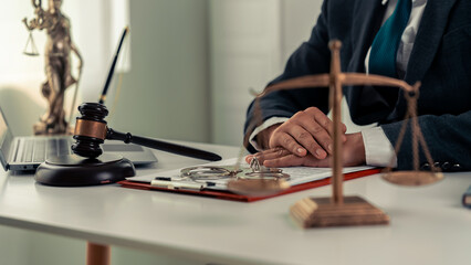 Close-up of lawyer sitting at desk with scale, hammer and small wooden toy house, working with...