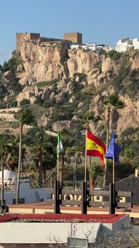 Flags of Spain, Andalusia and the European union waving together in the wind with the view of Salobrena castle in the Background, Spain.