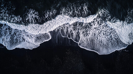 Aerial view of ocean waves crashing on a black sand beach creating white foam patterns on the shore