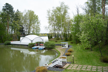 View of the path leading to the pond with a festive white tent and catamarans, surrounded by trees