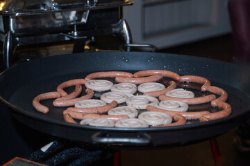 Various sausages are fried in a giant frying pan to prepare hot appetizers for the guests of the holiday.
