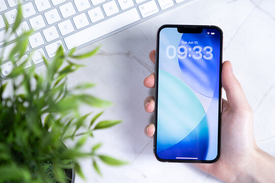 Poznan, Poland - June 10, 2025: Hand holding a modern smartphone displaying the new iOS 26 lock screen featuring an innovative Liquid Glass design